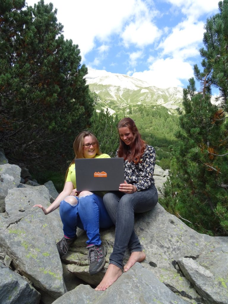 Kuvassa kaksi naista istuu kallioilla läppärin äärellä.
